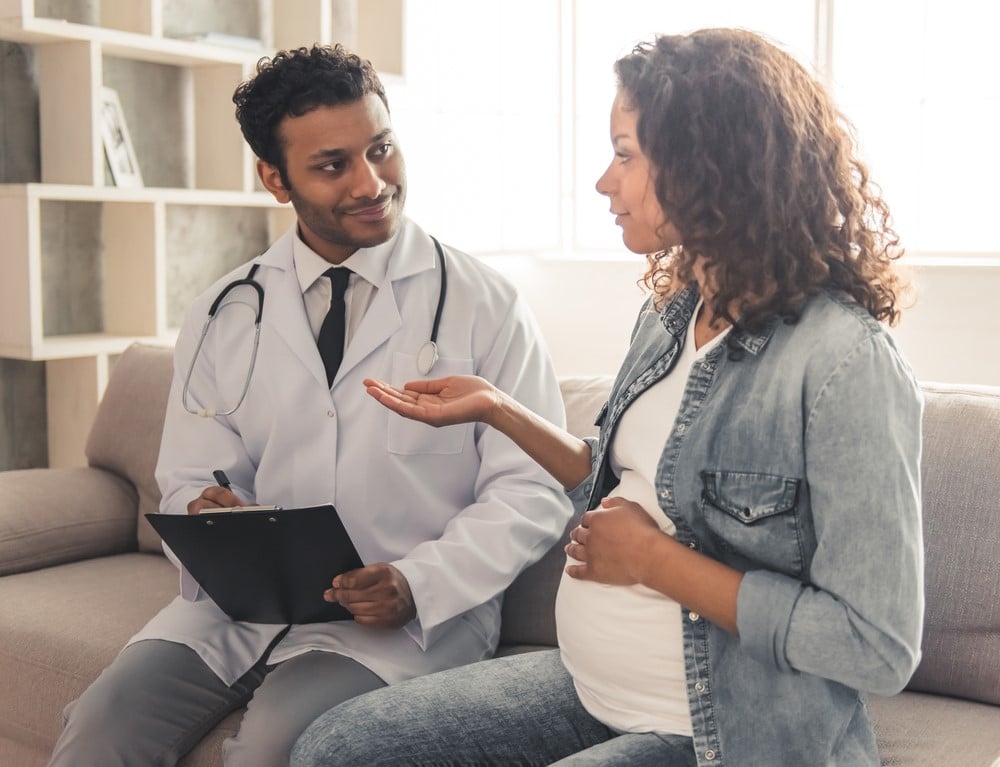Pregnant woman smiling while speaking with her supportive doctor during a prenatal appointment