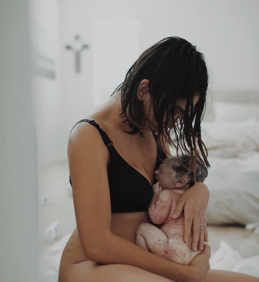Hypno-mom Adriana with her head bowed holding her newborn baby covered in vernix