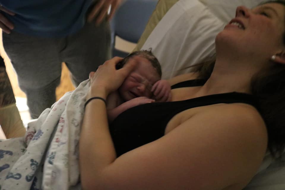 Hypno-mom just after giving birth with a look of joy on her face and holding her new baby on her chest.