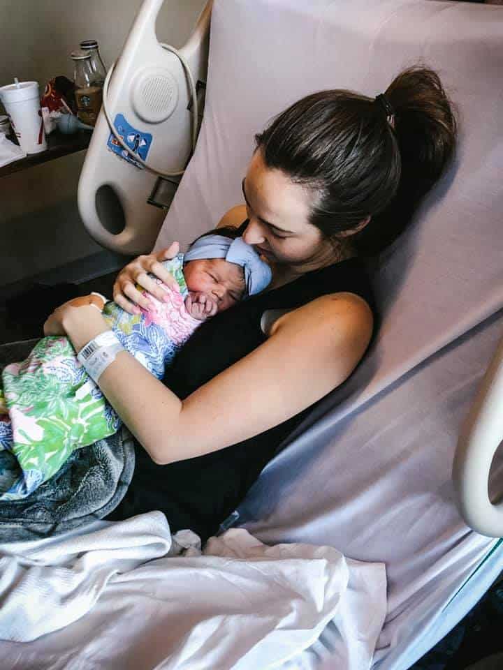 Hypno-mom Allie holding swaddled newborn baby with a blue bow in her hospital bed