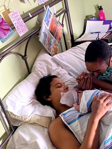 Hypno-mom laying in bed skin to skin with newborn and holding hands with partner