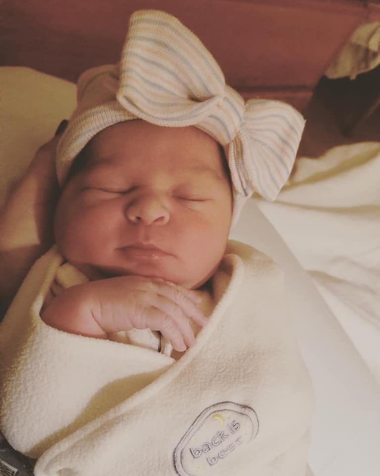 Hypno-mom Ashley's newborn daughter swaddled and wearing a hospital hat with a bow