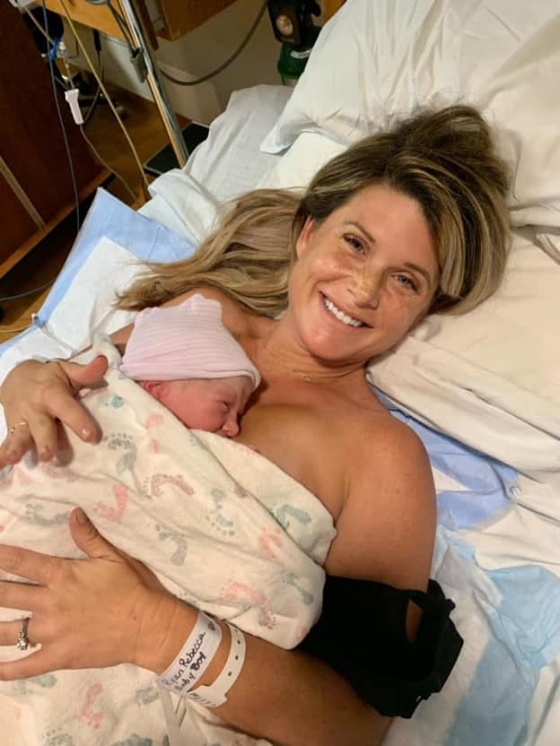 New parent skin to skin with newborn and smiling at camera