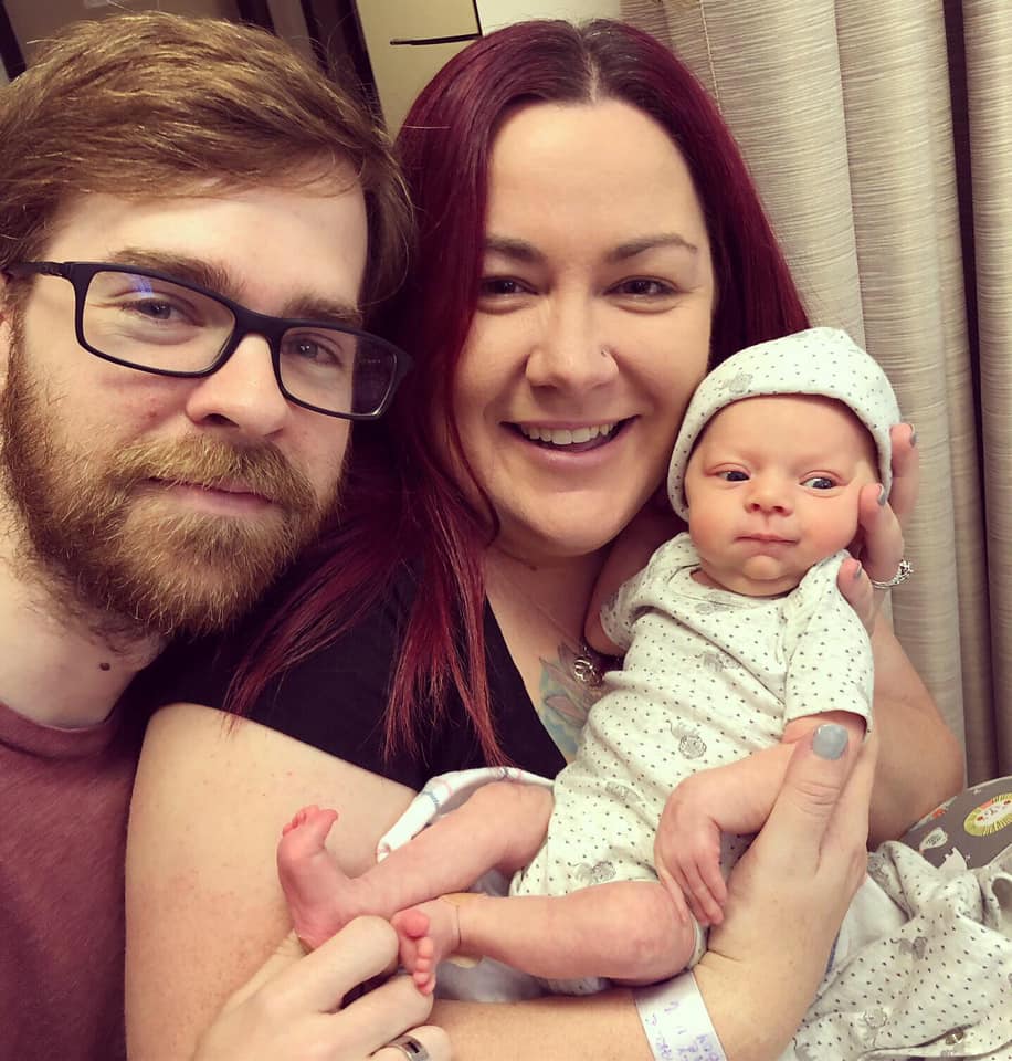 Hypno-mom Carlee, partner Leo holding up their newborn baby.