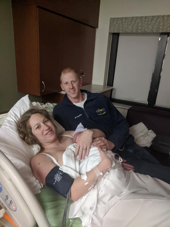 Hypno-mom Cassie, birth partner and newborn in hospital bed smiling.