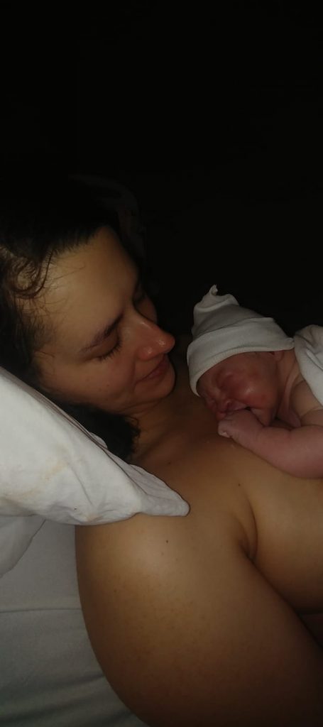 New parent skin to skin with newborn baby wearing a hat