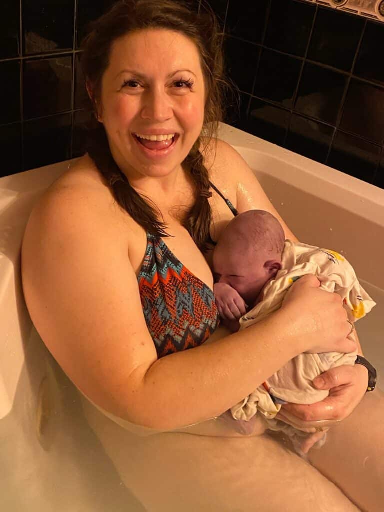 New parent in tub smiling and holding newborn
