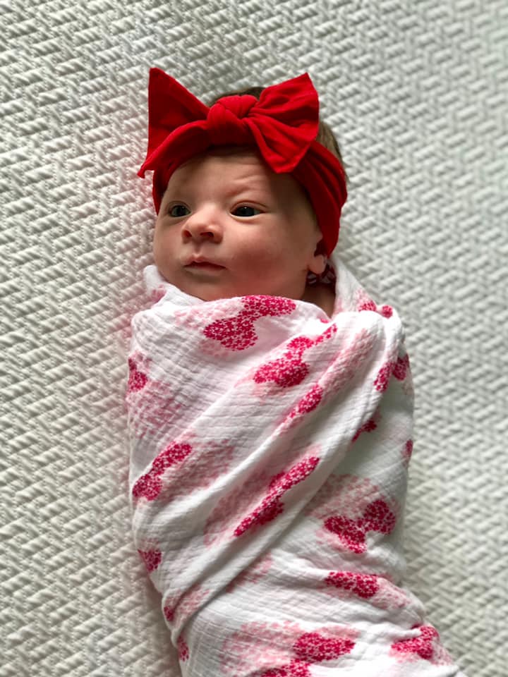 Hypno-mom Cheryl's baby swaddled in a pink and white blanket with a big read headband with a bow.