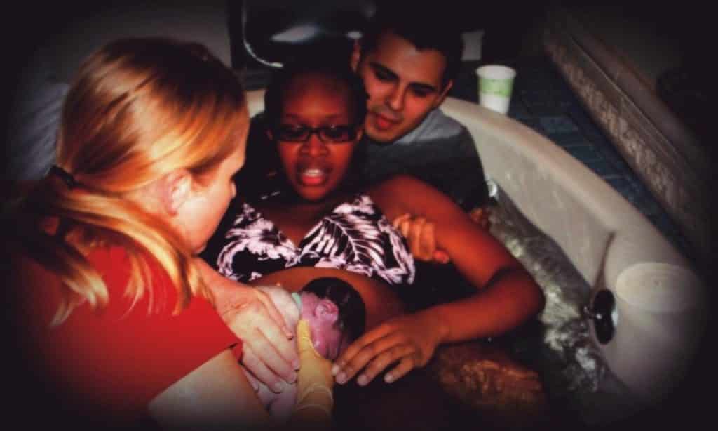 Hypno-mom Christine, partner and midwife handing her newborn baby to her in the birth tub just after birth