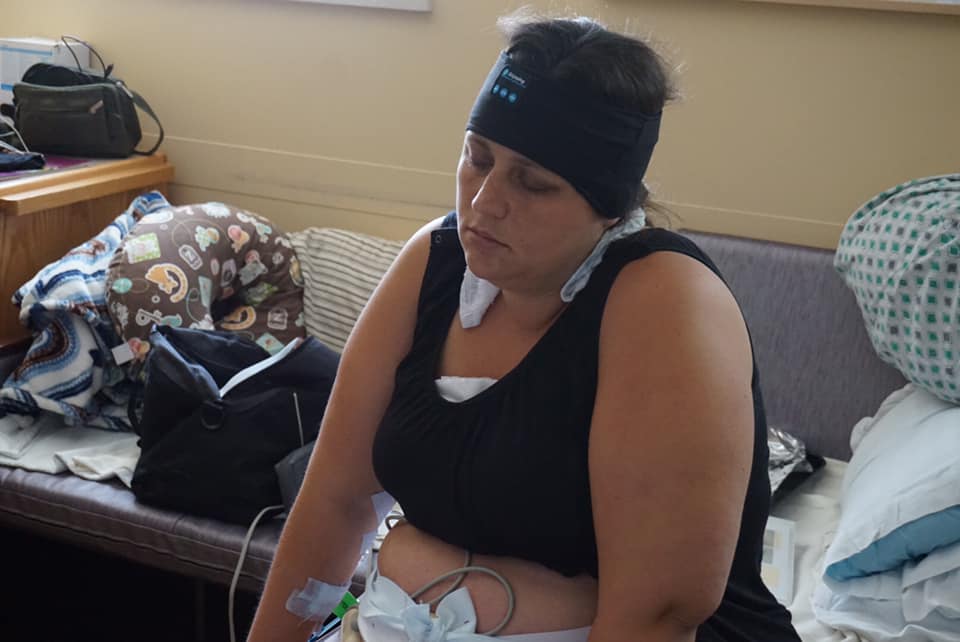 Hypno-mom Hanna sitting in the hospital with the monitors on and her eyes closed listening to her hypnosis tracks with her Zenband on and washcloth around her neck.