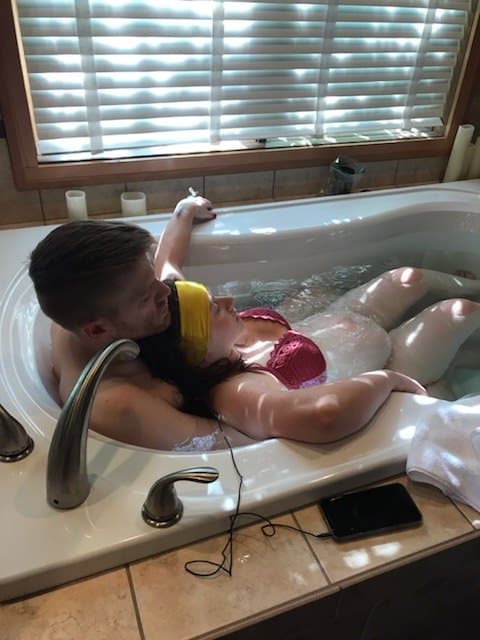 Hypno-mom Jen leaning against her birth partner in the birth tub listening to her hypnosis tracks and wearing her zen bands.
