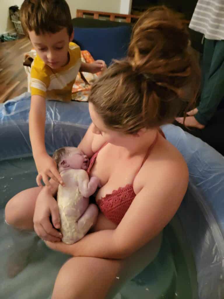 new parent in tub with newborn and other children watching