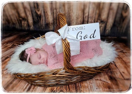 Baby in a basket with a pink bow and blanket and a sign that says from God