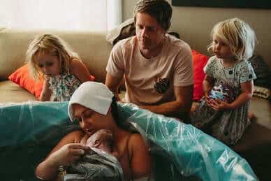birthing person holding newborn in birth tub with family watching