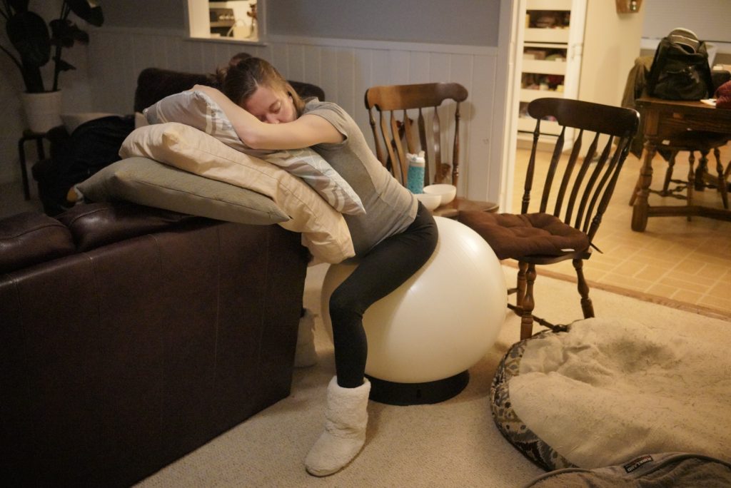 Hypno-mom Karin at home sitting on birth ball at the edge of the couch leaning over pillows.