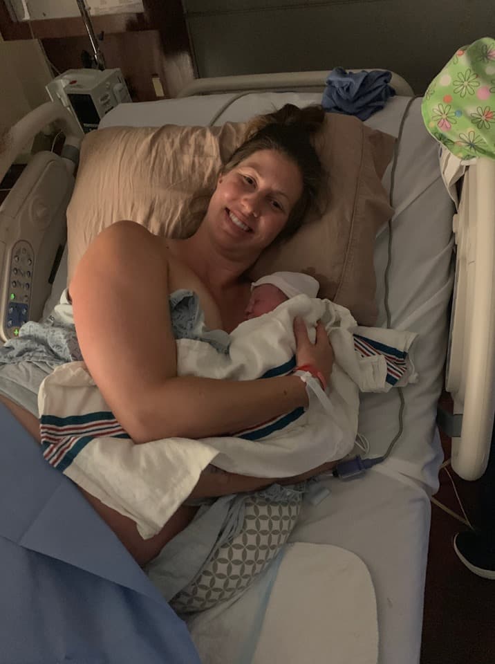 Lauren laying on her side in the hospital bed holding her newborn baby and smiling.
