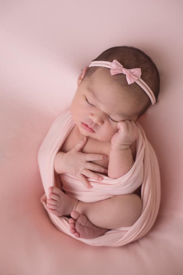 Hypno-mom Lina's newborn wrapped in a pink blanket with a pink bow in her hair.