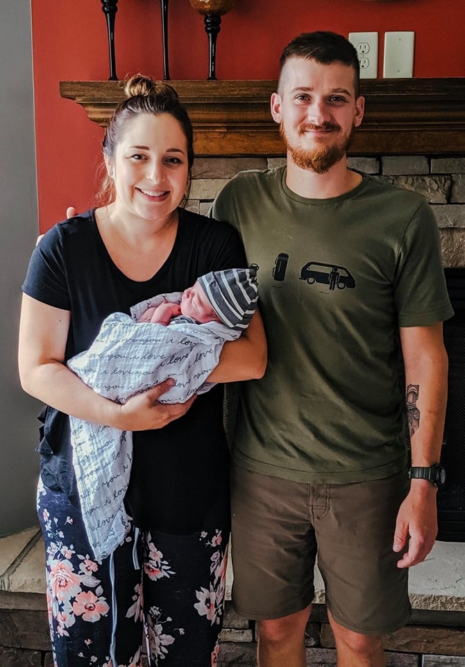Hypno-mom Lindsey and husband standing in front of fireplace holding their newborn