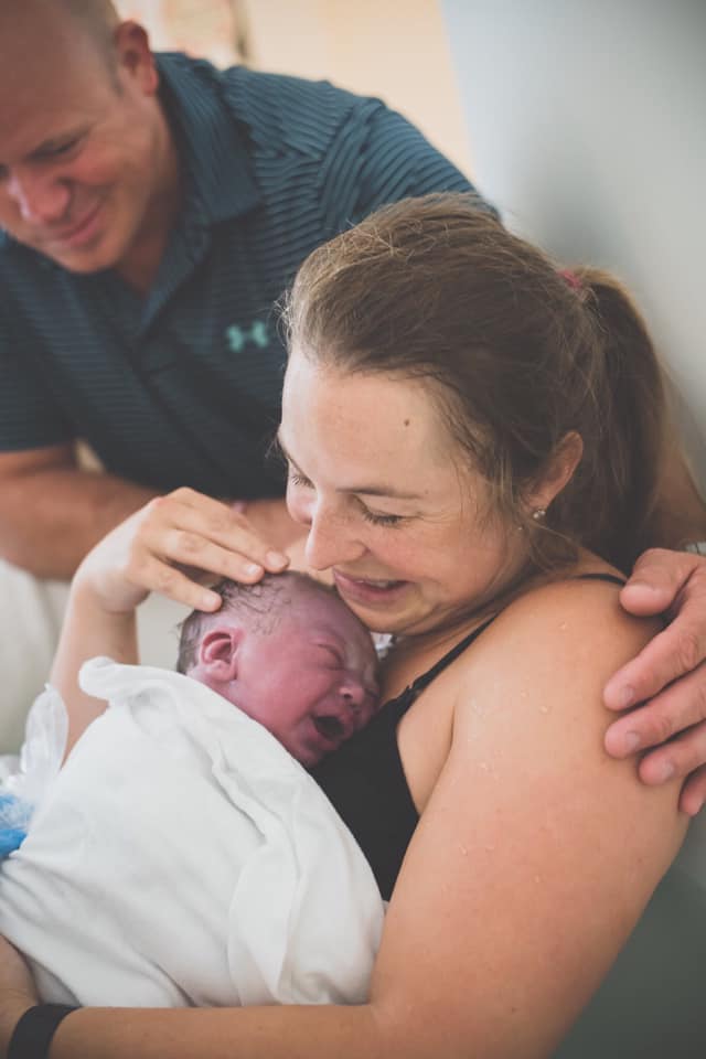 Hypno-mom Meagan crying and welcoming her newborn baby with birth partner's arm around her.