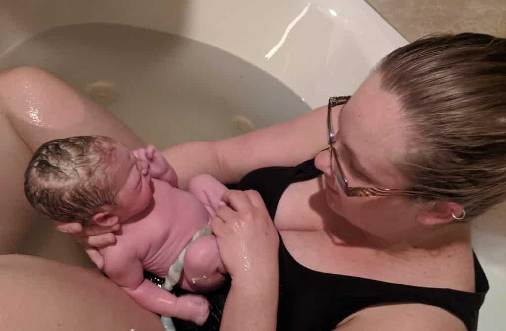 Hypno-mom in birth tub gazing at newborn baby with umbilical cord still attached.