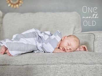 one month old baby laying on chair with a grey striped blanket