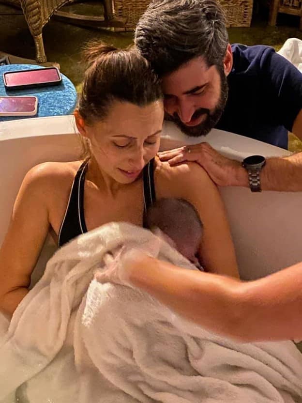 Hypno mom in tub with newborn and partner looking over her shoulder