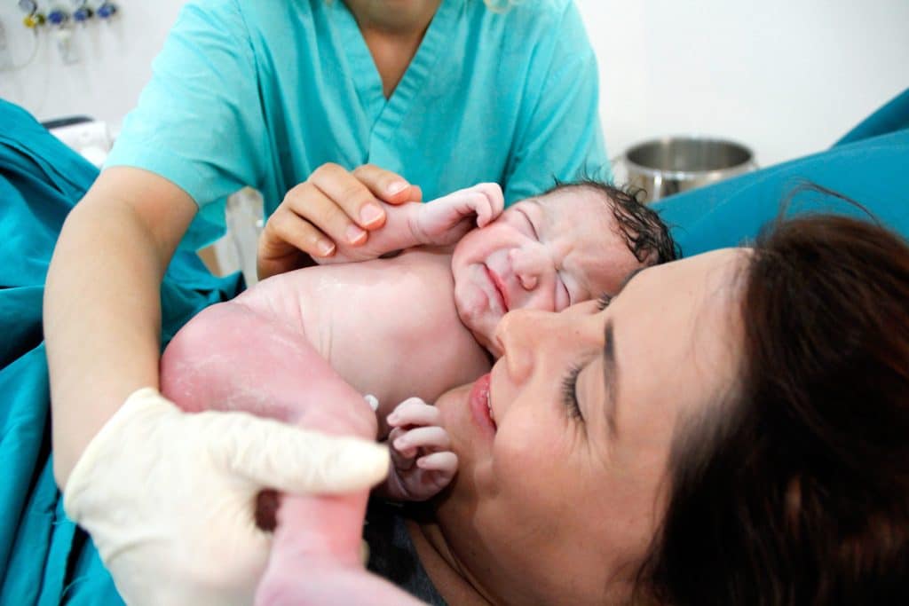 A joyful mother smiles as she receives her newborn from the doctor immediately after a cesarean birth.