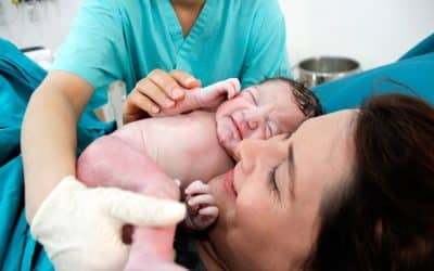 A joyful mother smiles as she receives her newborn from the doctor immediately after a cesarean birth.