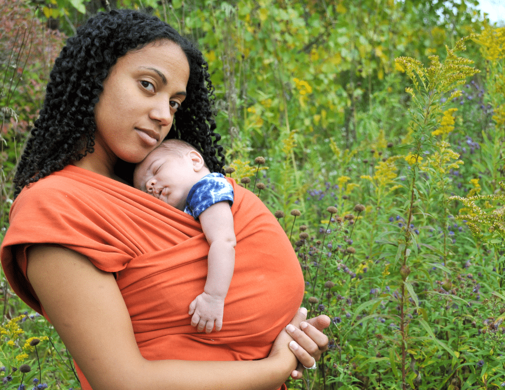 Mother wearing her sleeping newborn in a sling wrap across her chest.