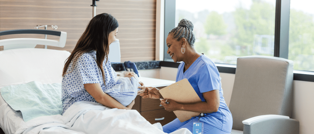 Midwife sitting beside a new mother holding her newborn baby, offering support and care after birth.