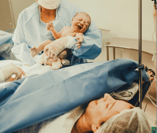 A joyful mother smiles as she sees her newborn from the doctor immediately after a cesarean birth.