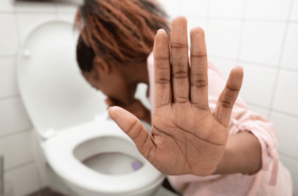 Pregnant woman experiencing severe nausea, covering her mouth to prevent vomiting.