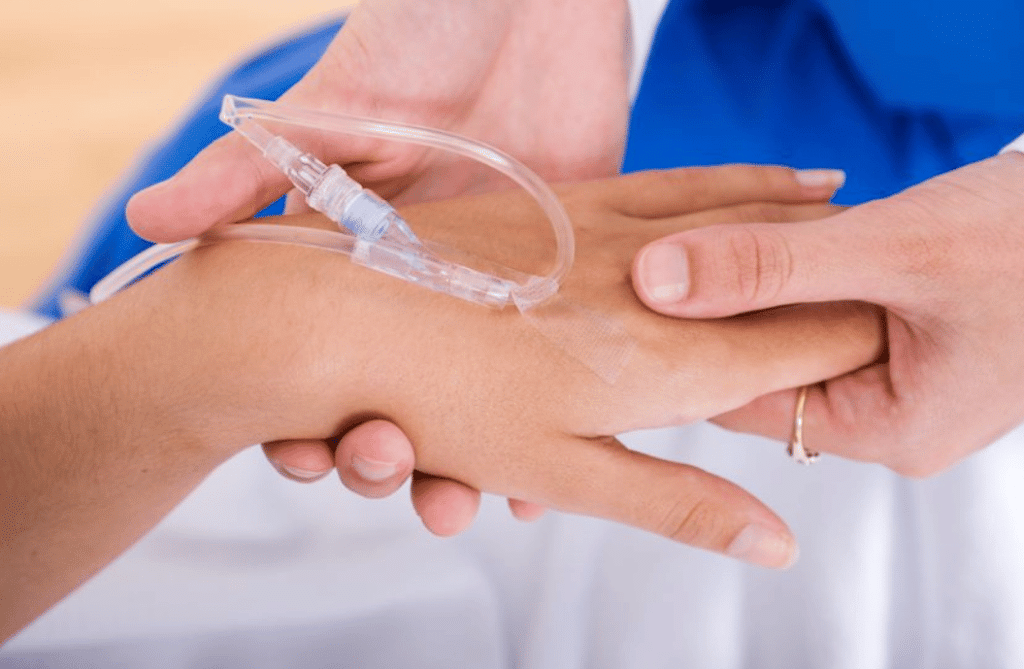A nurse inserts a continuous IV into the back of a pregnant woman’s hand during hospital admission.