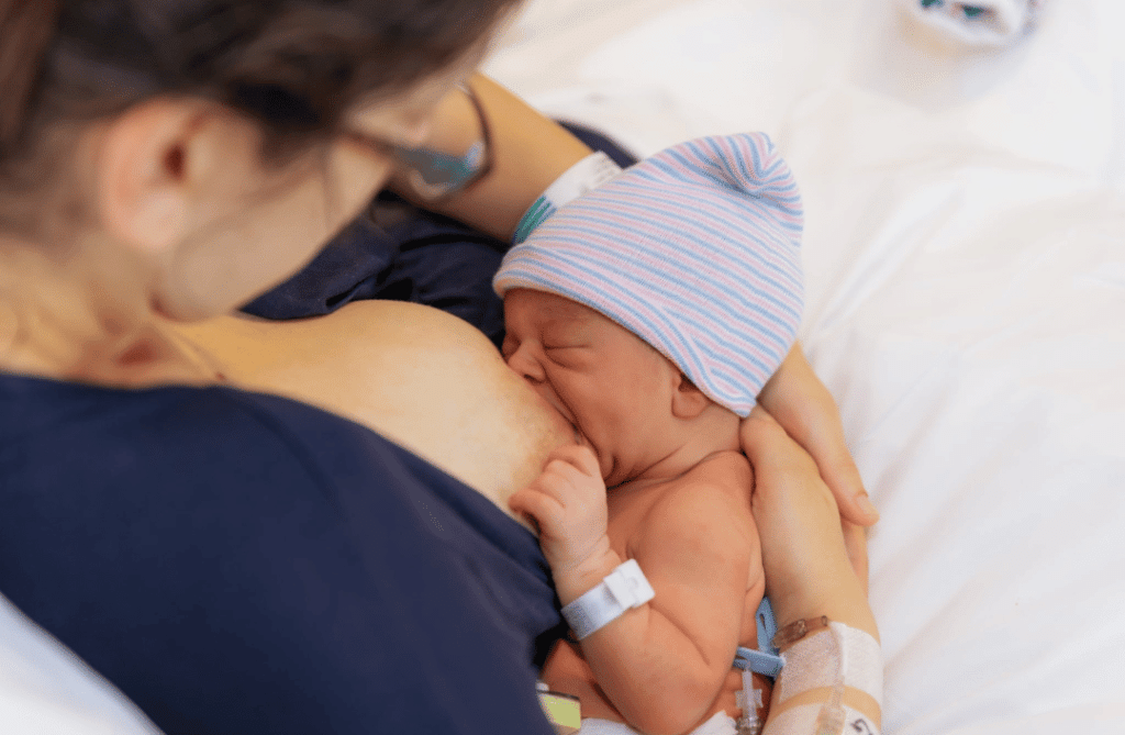 Newborn baby breastfeeding, held closely in mother’s arms in a hospital setting.